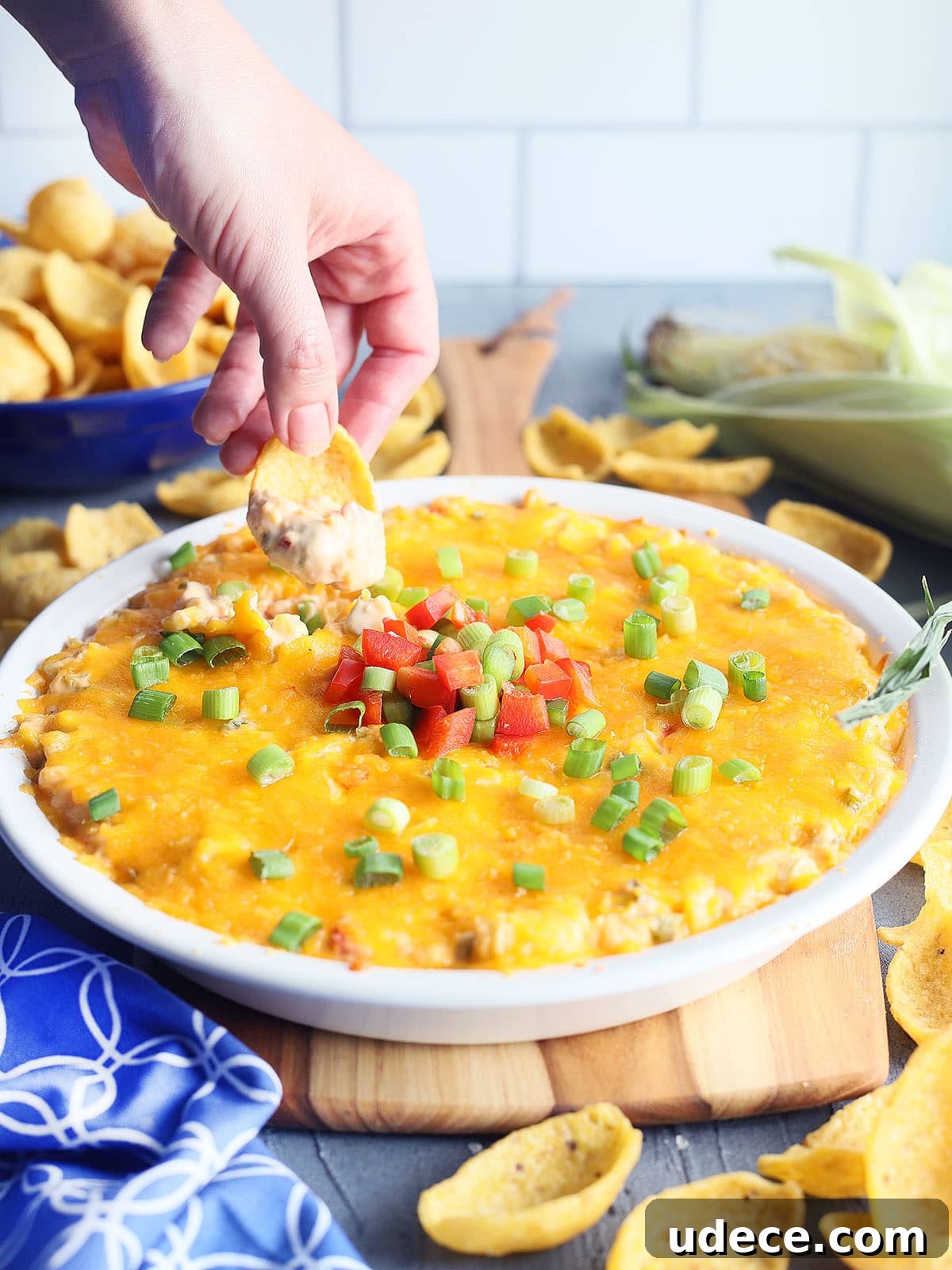 hand dipping a corn chip into a dish of hot corn dip with cream cheese