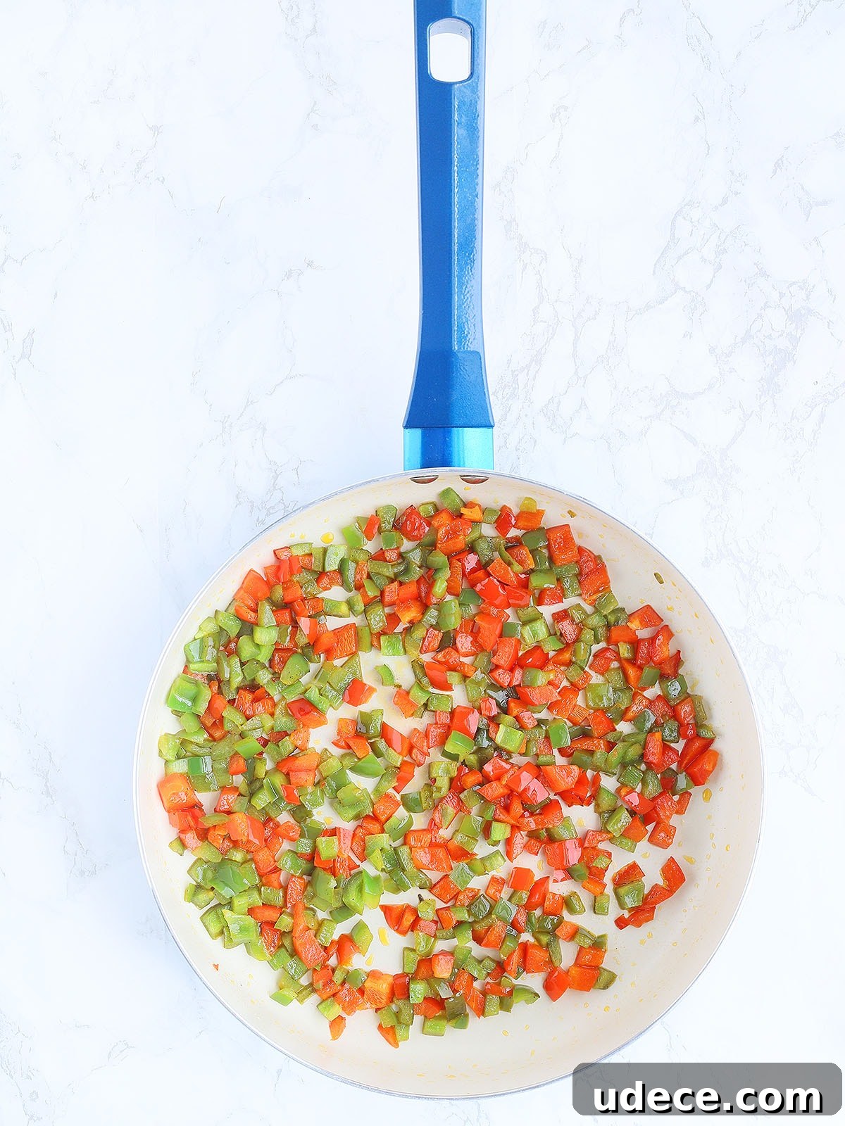 sauteed red and green diced bell peppers in a large blue skillet