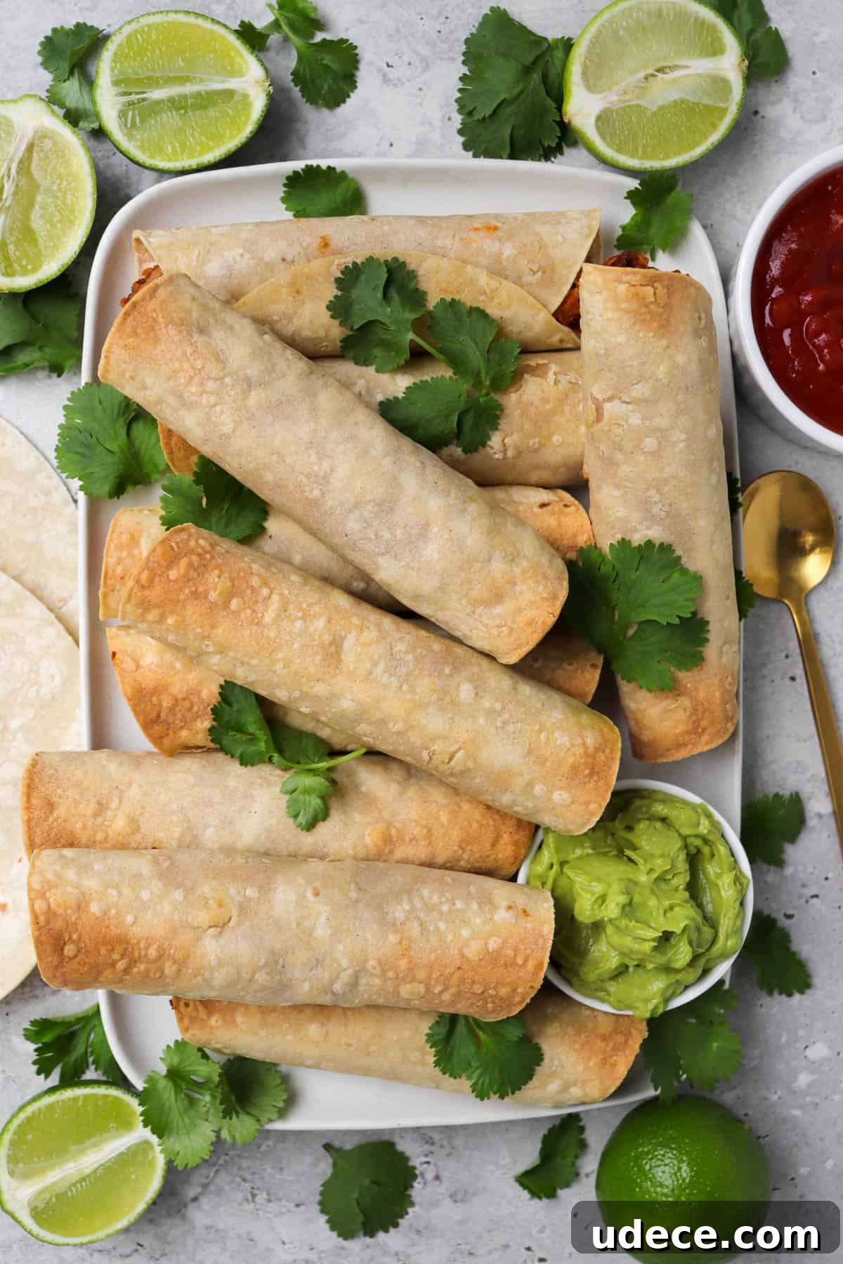 Vegan Lentil and Roasted Cauliflower Taquitos Recipe 4 Taquitos on a platter garnished with coriander, side of guacamole, halved limes, gold spoon and salsa on the side.