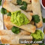 Taquitos on platter topped with coriander leaves and guacamole. Fresh cut up limes, tortillas, salsa and gold spoon on the sides.