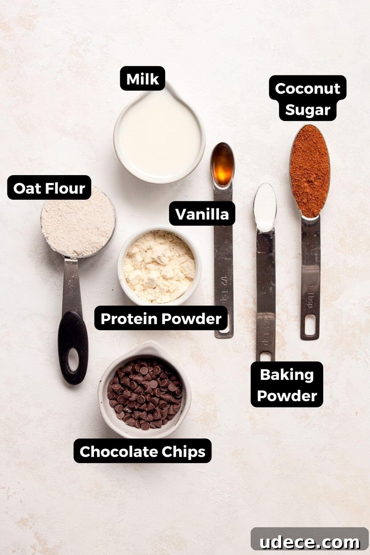 Protein Powder Mug Cake Recipe — Quick Single-Serve Dessert 3 All ingredients in one minute protein mug cake recipe in small bowls including protein powder, oat flour, vanilla extract, coconut sugar, baking powder, milk, and chocolate chips.