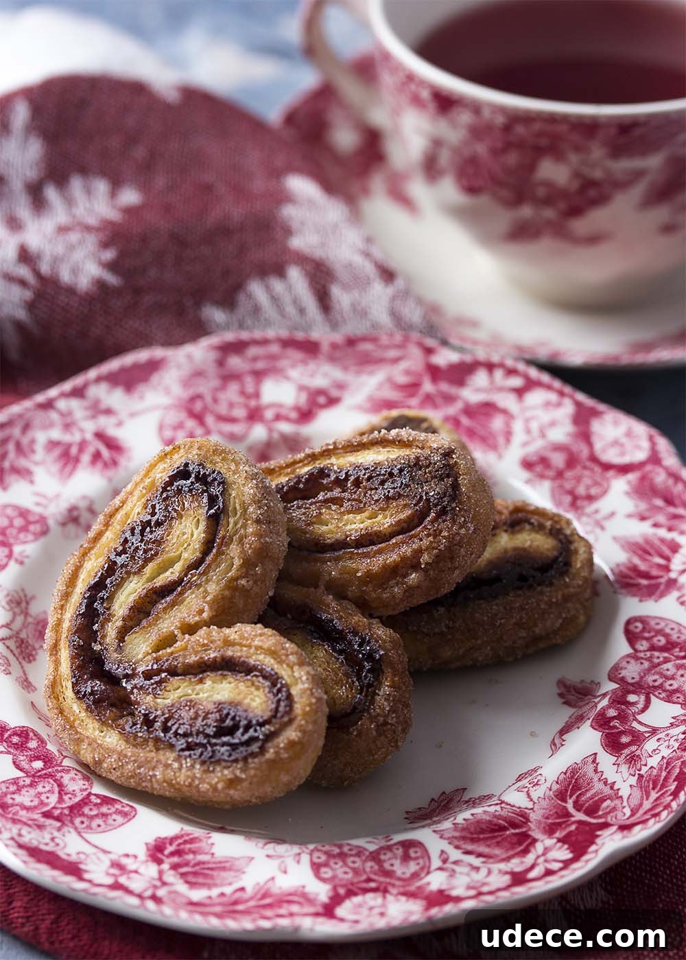 Cinnamon cocoa palmiers arranged on a plate with a cup of tea in the background.