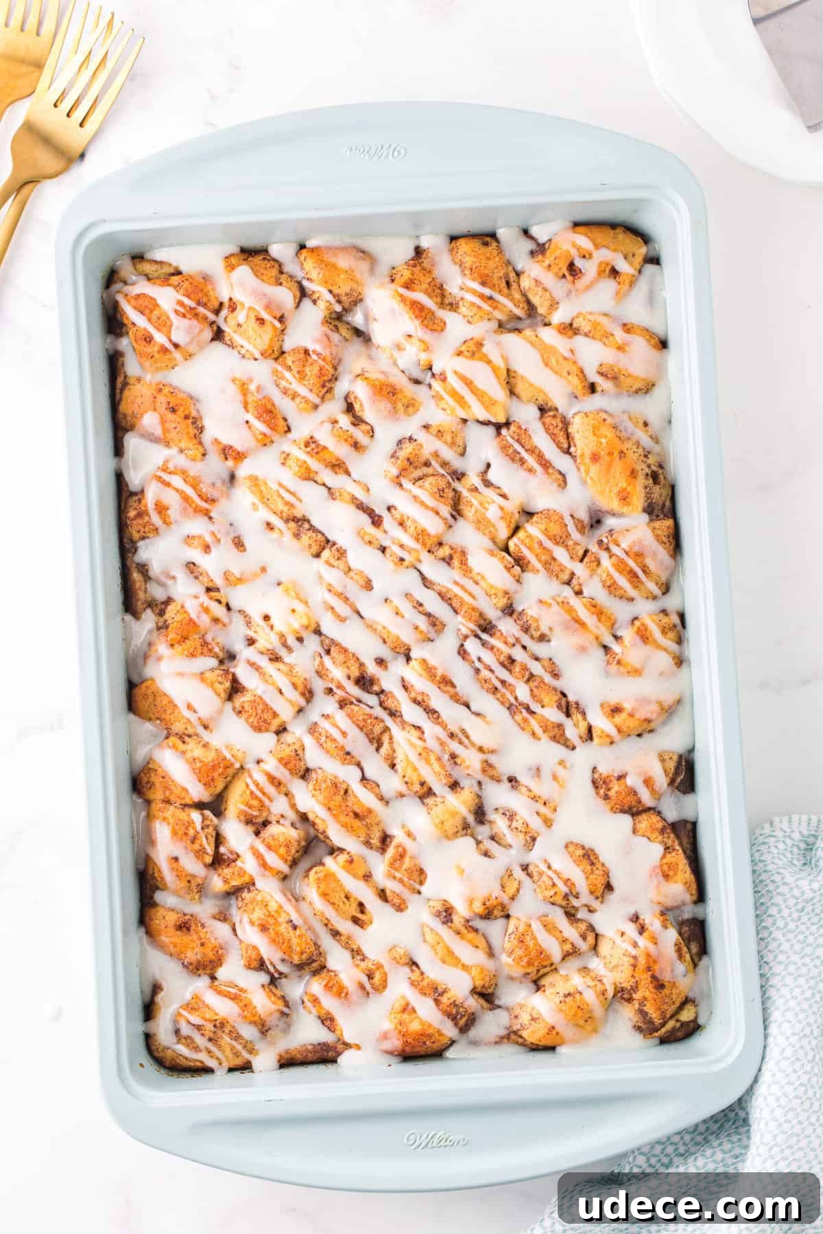 cinnamon roll casserole with icing drizzled on top in light blue baking dish
