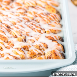 A close-up of a cinnamon roll casserole showcases golden-brown rolls packed together, generously drizzled with white icing.