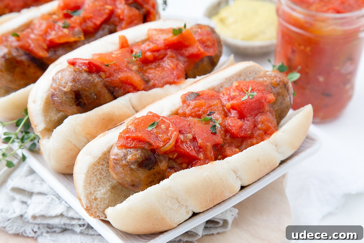 Homemade Tomato Jam Recipe: Sweet & Savory Preserving Guide 7 bratwursts on buns topped with tomato jam, sitting on a white platter