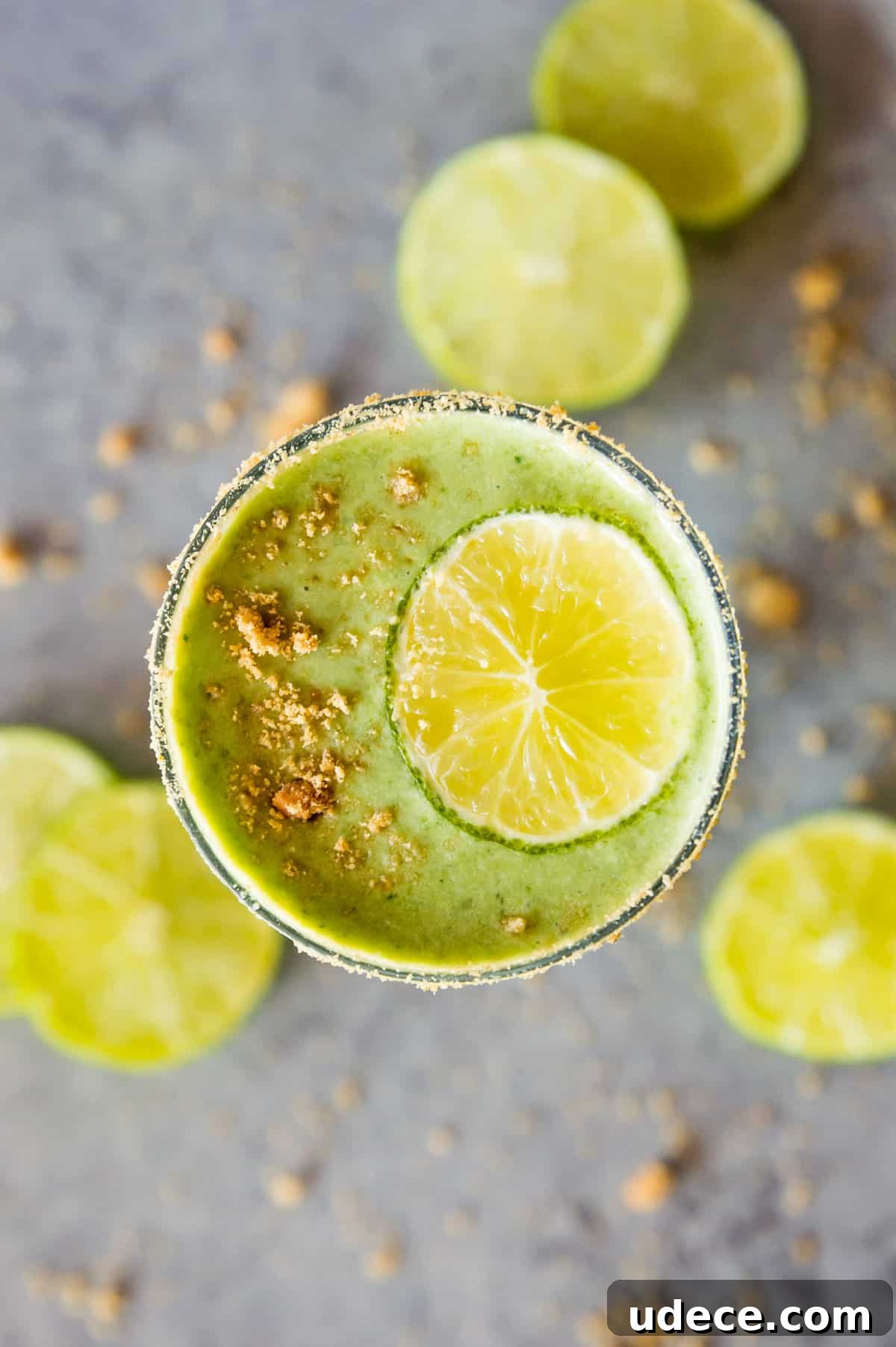 A key lime pie smoothie in a glass topped with crushed graham cracker crumbs and a lime slice.