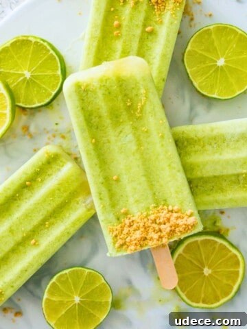 Four key lime pie popsicles stacked on top of each other with lime wedges around them.