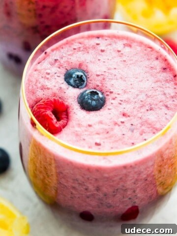 A glass of berry lemonade smoothie topped with fresh blueberries and raspberries.
