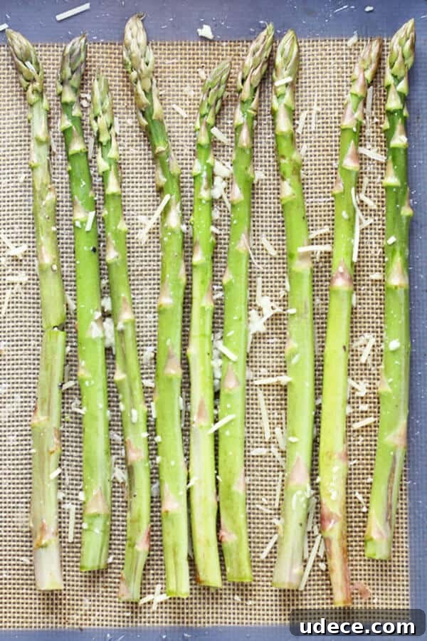 Roasted Lemon Garlic Asparagus Recipe for Crispy Tender Spears 4 raw asparagus spears laid out in a single layer on a baking tray covered in parmesan cheese and minced garlic