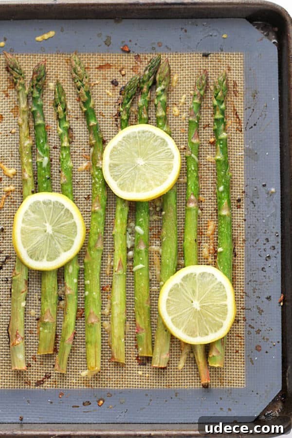 Roasted Lemon Garlic Asparagus Recipe for Crispy Tender Spears 5 asparagus spears laid out in a single layer on a baking tray covered in parmesan cheese, minced garlic and lemon slices