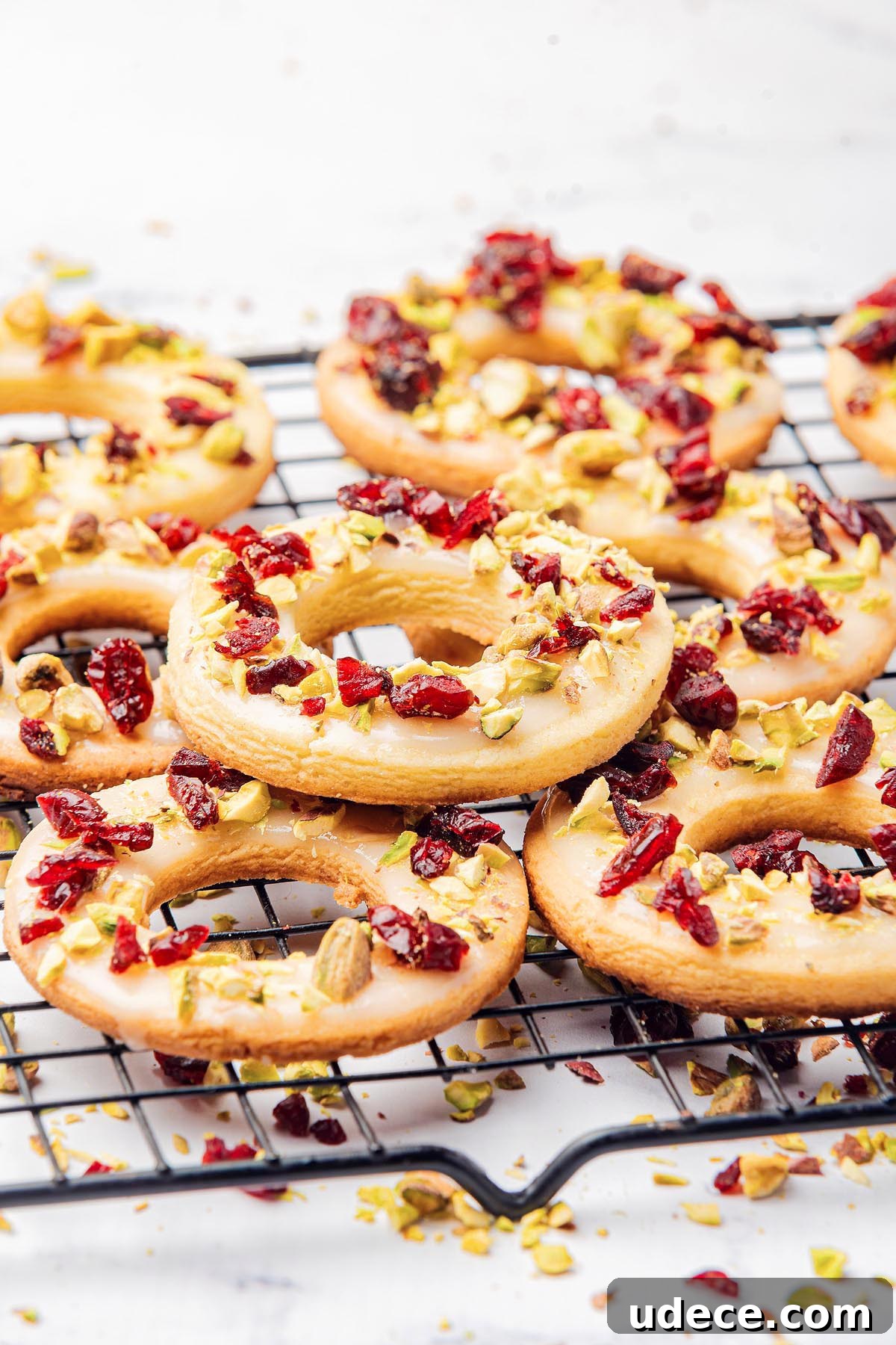 Cranberry Pistachio Holiday Wreath Cookies Recipe 6 Cranberry pistachio wreath cookies rest on a cooling rack, adorned with vibrant dried cranberries and finely chopped pistachios.