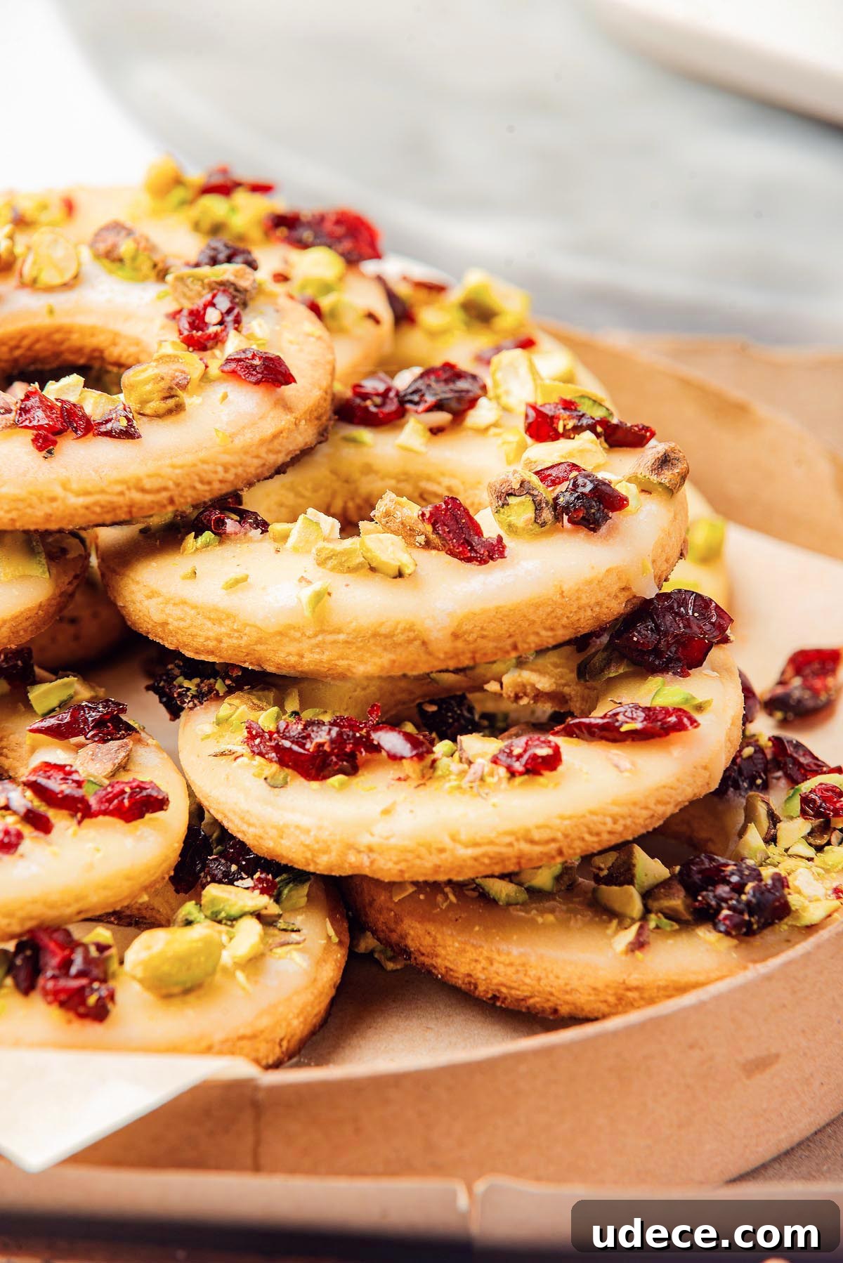 Cranberry Pistachio Holiday Wreath Cookies Recipe 7 A stack of cranberry pistachio wreath cookies, glazed and topped with chopped pistachios and dried cranberries, sits invitingly on a parchment-lined tray.