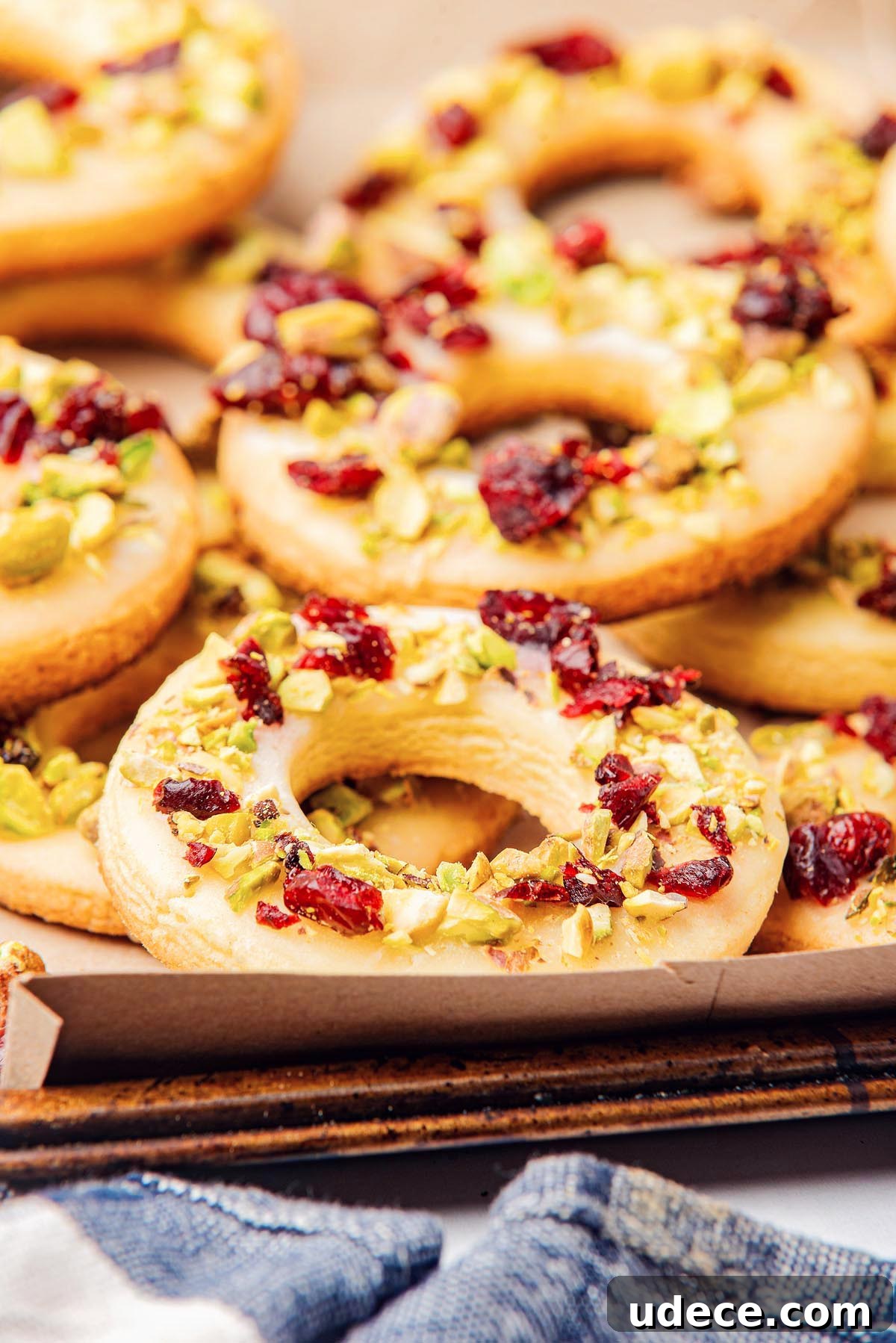 Cranberry Pistachio Holiday Wreath Cookies Recipe 10 Close-up of cranberry pistachio wreath cookies topped with chopped pistachios and dried cranberries on a baking tray.