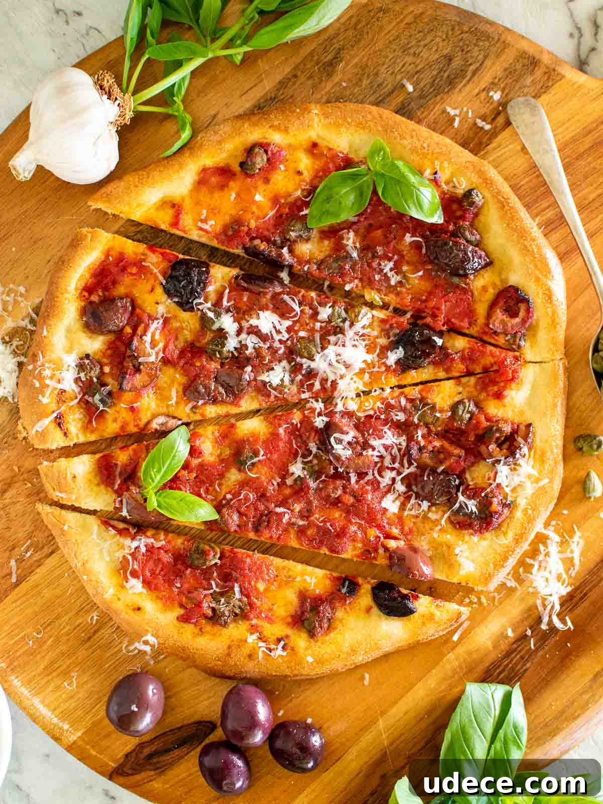 Calabrese Pizza: Spicy Italian Pepperoni & Calabrian Chili Recipe 2 pizza with tomatoes, black olives, anchovies and capers with sprinkling of parmesan cut into four pieces viewed from above.