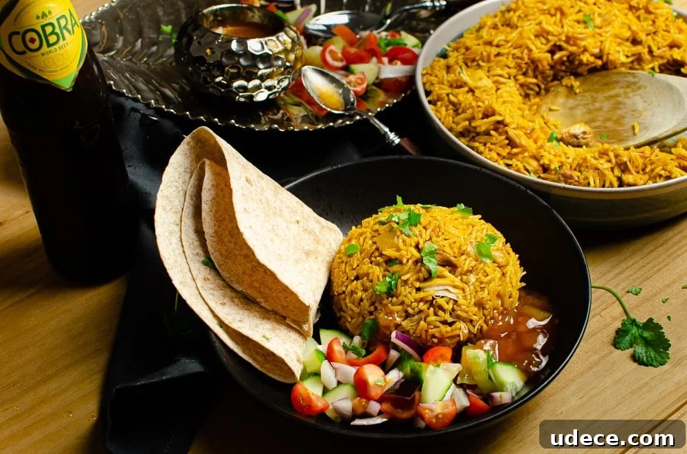 Authentic Pressure Cooker Chicken Biryani Recipe – Ready Fast 12 Pressure cooker Chicken Biryani served in a green bowl with chopped coriander on top, salad, mango chutney,Chapati and a bottle of cobra beer served on the side