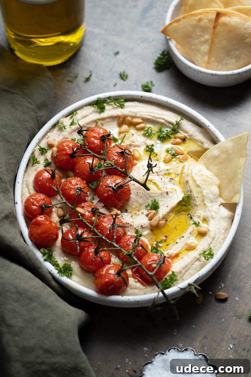 Hummus with roasted vine tomatoes in a white bowl with a chip dipped in the side.