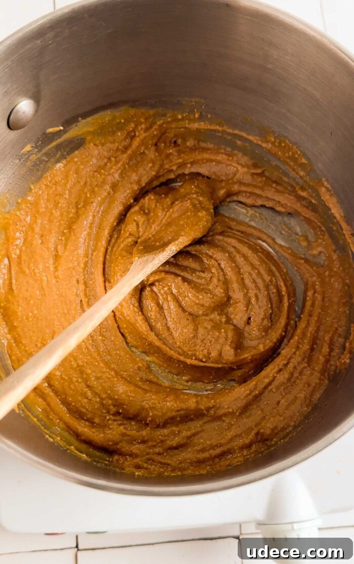 Homemade Butterfinger Candy Recipe Without Candy Corn 3 Peanut butter and maple syrup cooking in a small pot with a wooden spoon on it.