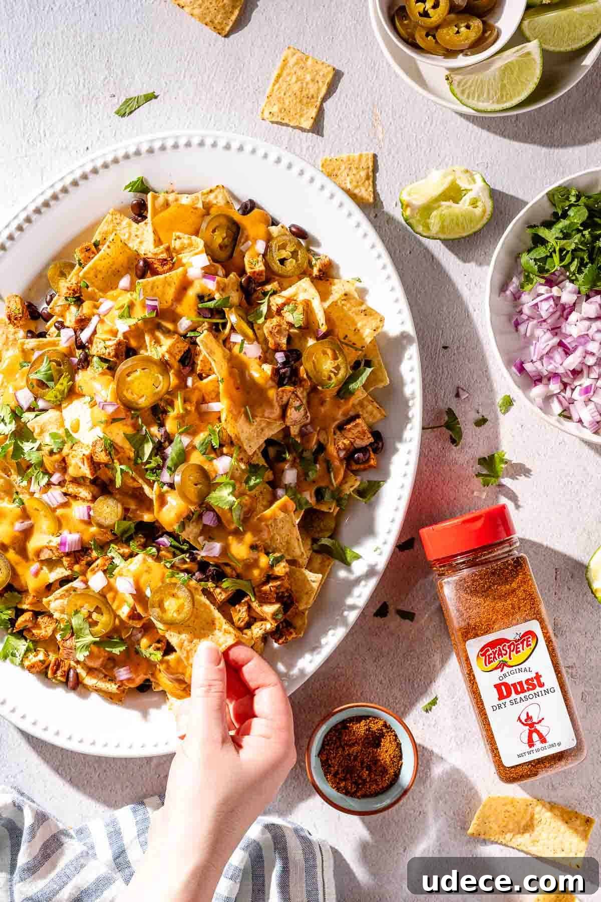 Spicy Queso Chicken Nachos Recipe for Game Night 2 hand taking nacho from platter with toppings on the side