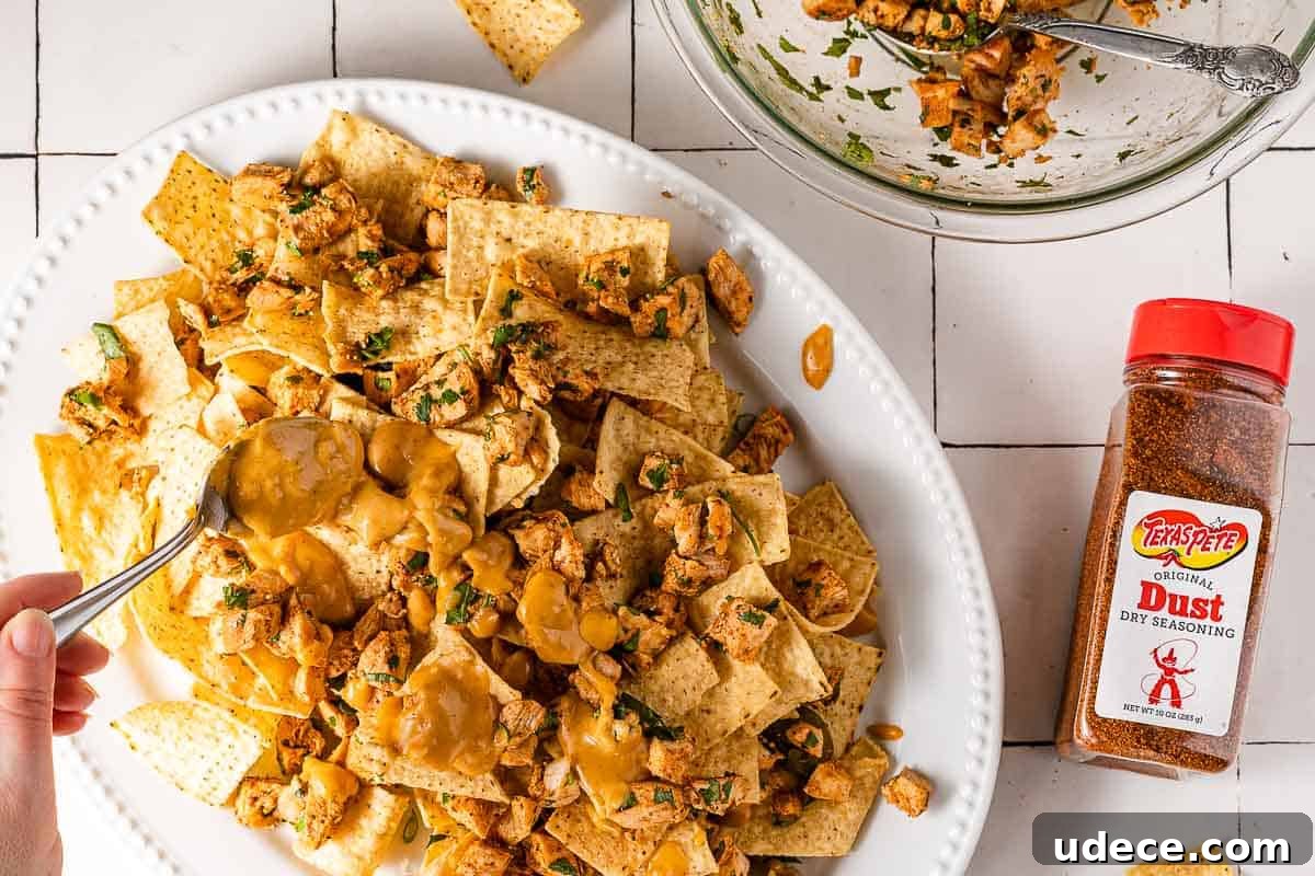 Spicy Queso Chicken Nachos Recipe for Game Night 7 spoon drizzling queso on platter of nachos