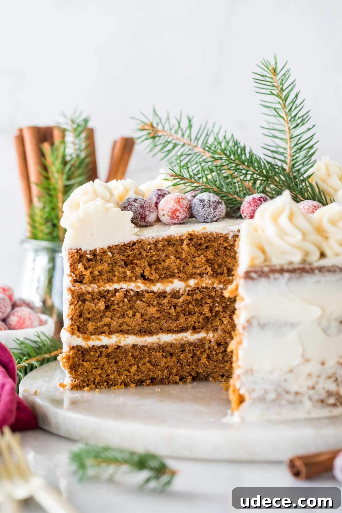 Gingerbread Layer Cake Recipe with Spiced Cream Cheese Frosting 8 Cross section of a three layer cake topped with sugared cranberries and evergreen sprigs.