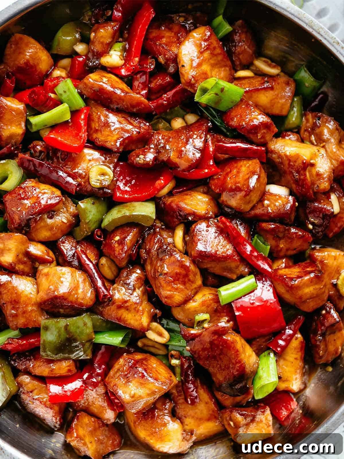 Close up image of Kung Pao Chicken in a sticky Kung Pao sauce with green and red chopped vegetables picked in with chicken pieces.