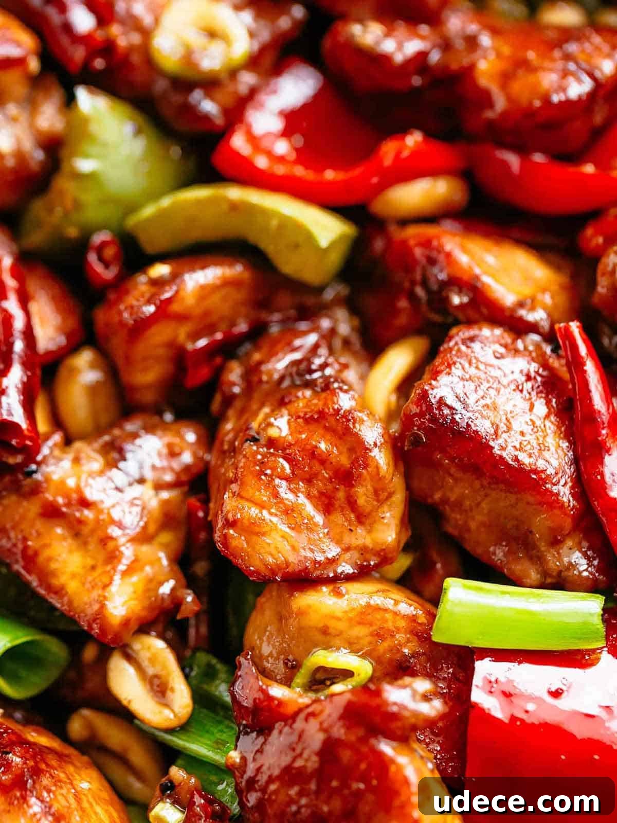 Close up image of Kung Pao Chicken in a sticky Kung Pao sauce with green and red chopped vegetables picked in with chicken pieces.