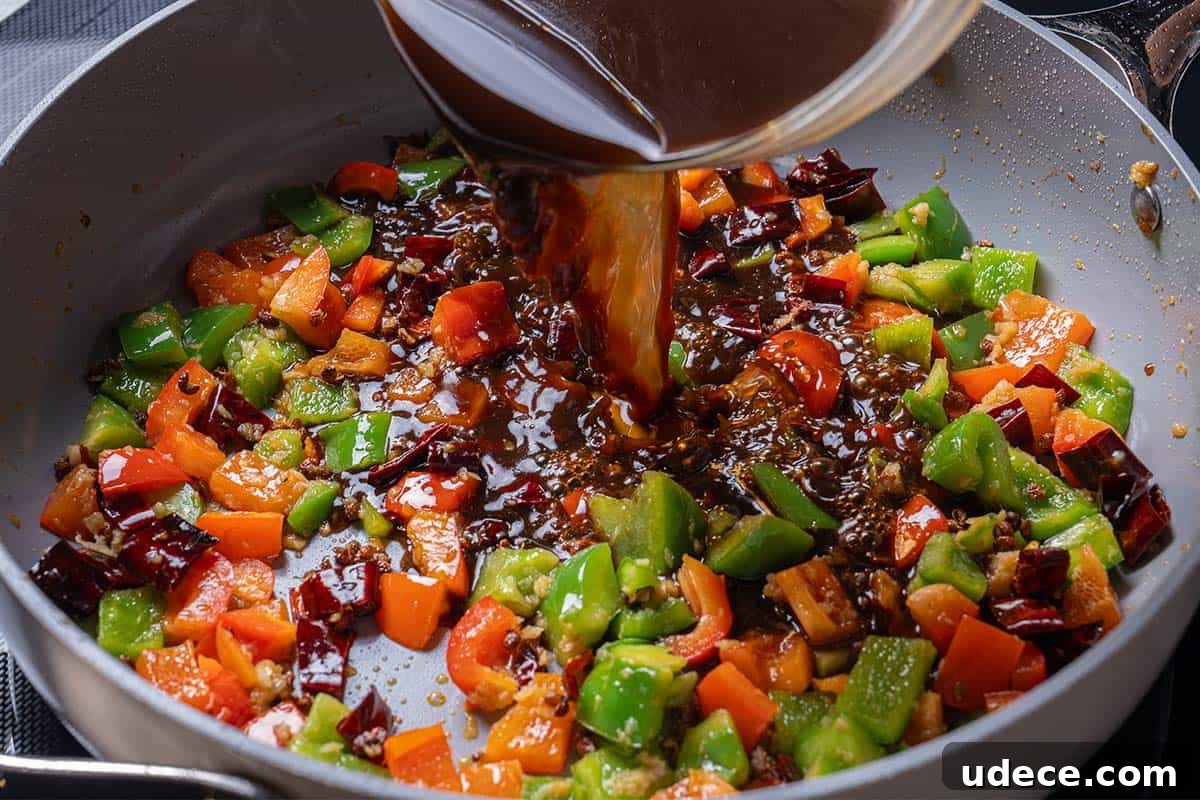 garlic, ginger, chili diced peppers (capsicums) and Sichuan peppercorns with a sauce mixture being poured into the wok