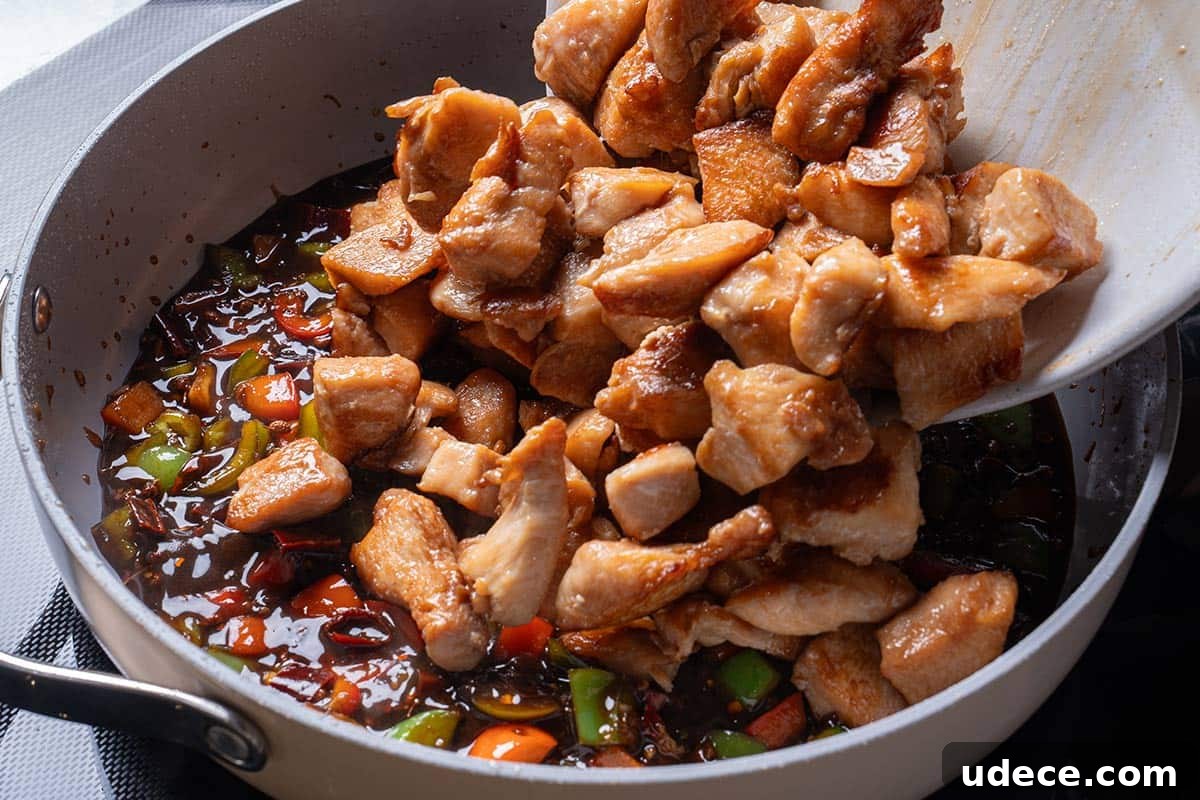 garlic, ginger, chili diced peppers (capsicums) and Sichuan peppercorns and sauce mixture with cooked chicken being poured in