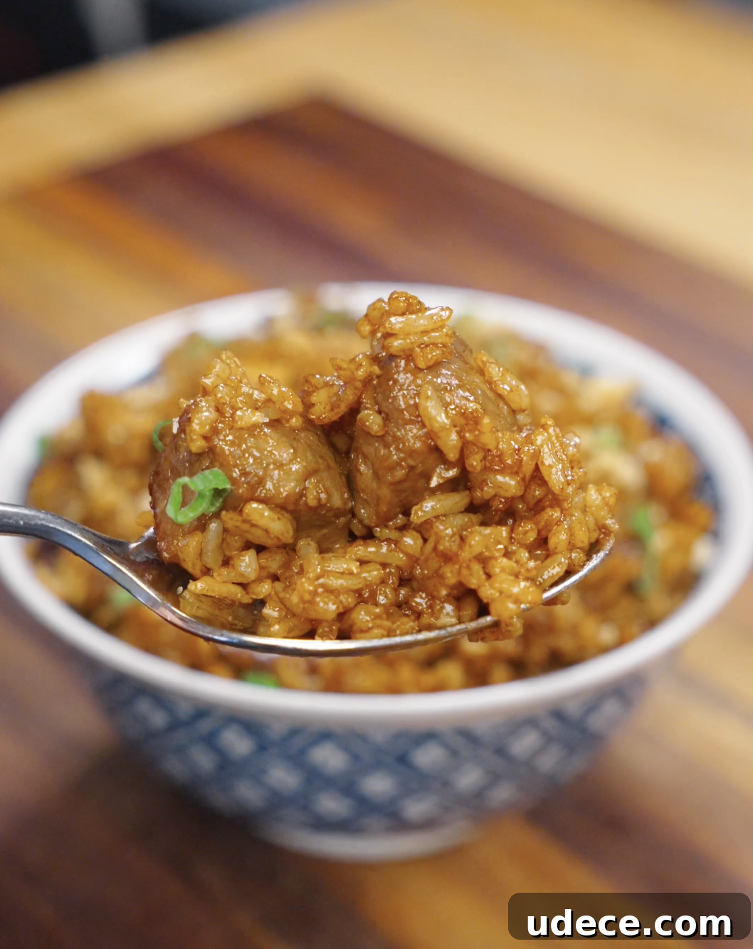 A spoonful of garlic beef fried rice being lifted, showing tender beef cubes and glossy soy-coated rice grains with a rich, savory finish.