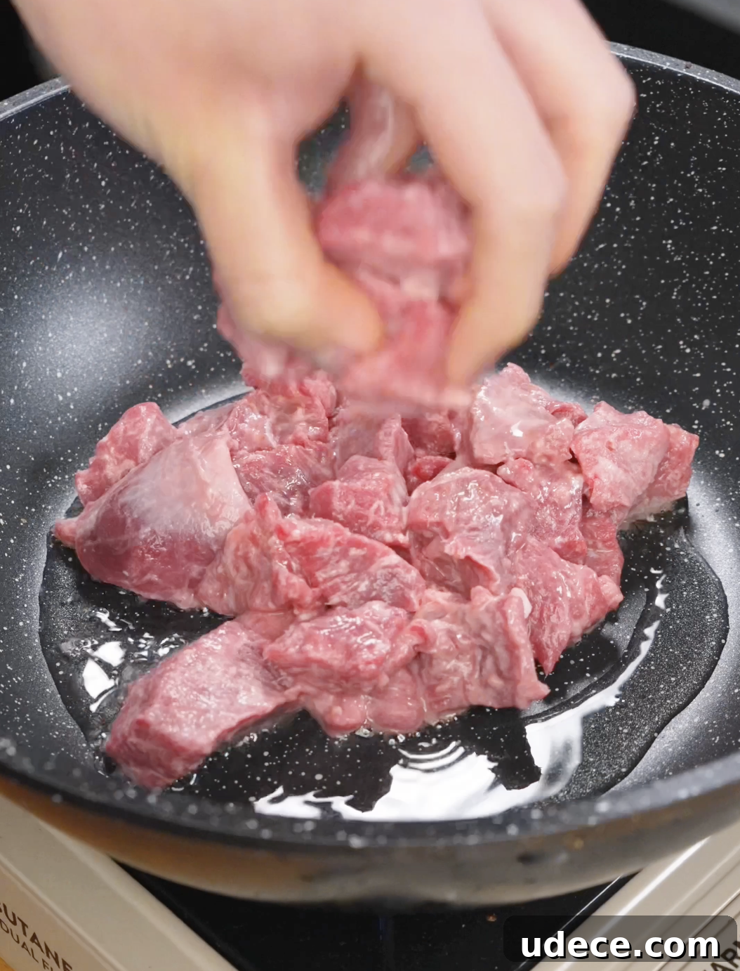 Marinated cubed sirloin beef being placed into a hot pan with oil, beginning the searing process to develop a browned crust for garlic beef fried rice.