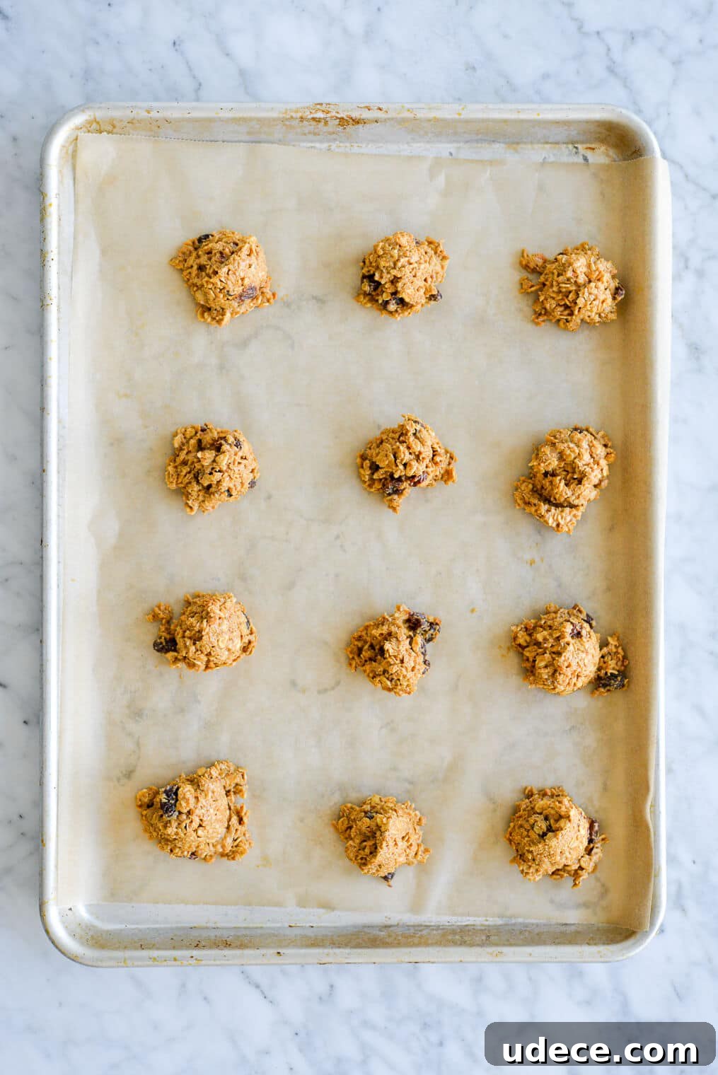 Scooped dough Oatmeal cookie dough scooped onto a parchment paper lined sheet pan in four rows of three.