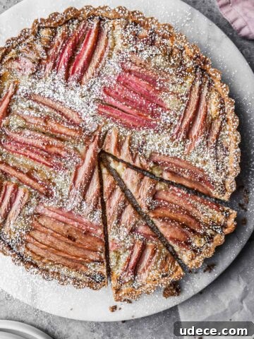 Rhubarb frangipane tart on a round marble platter with two slices cut.