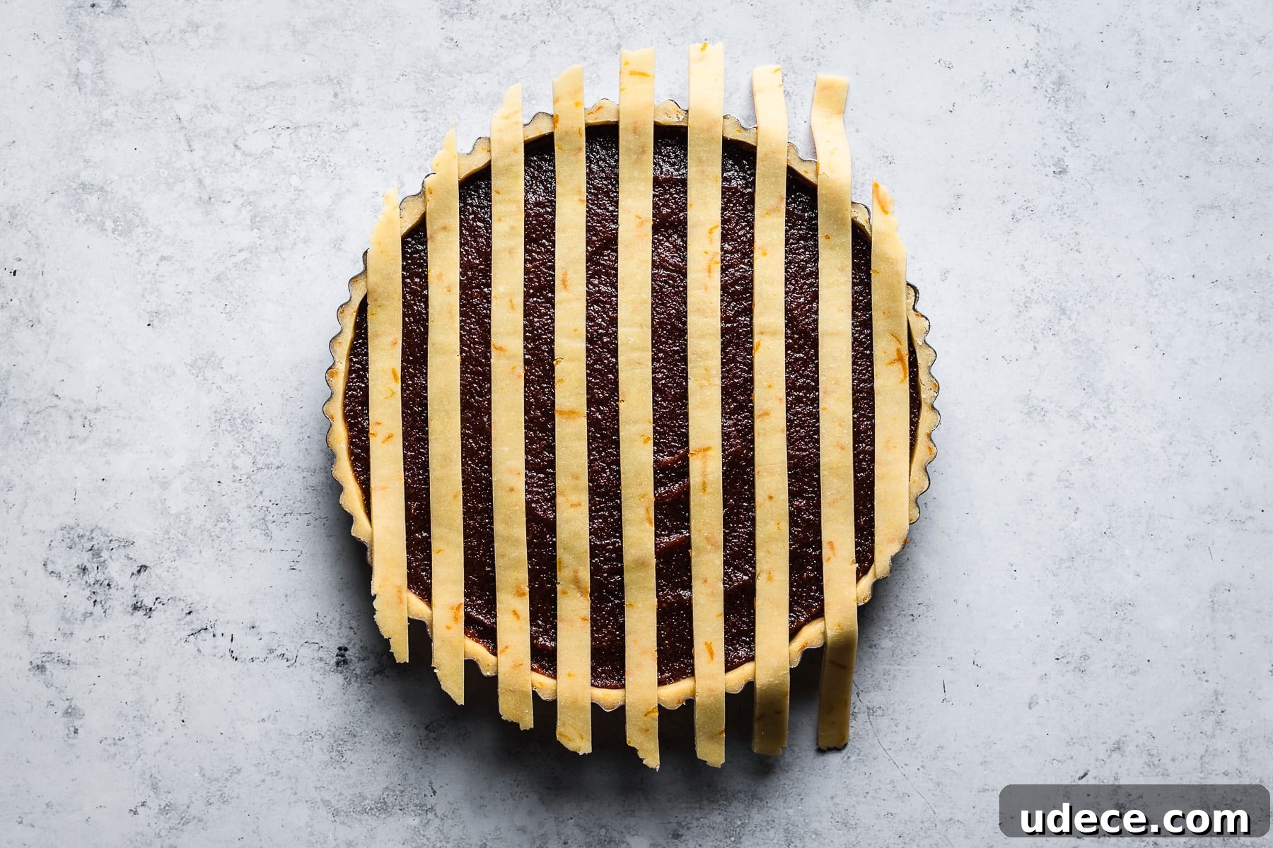Thin strips of lattice dough arranged vertically on a quince filled tart.