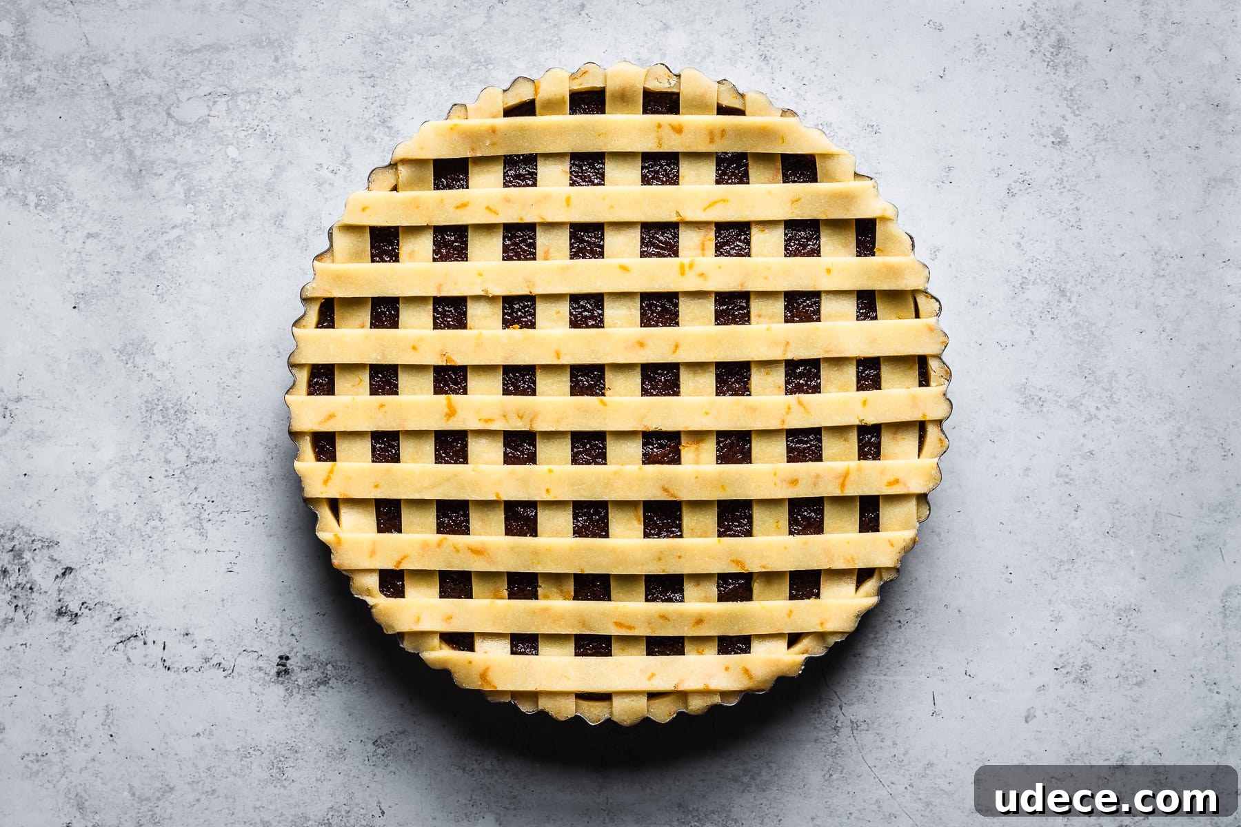 Thin strips of lattice dough arranged horizontally (with vertical strips underneath) on a quince filled tart.