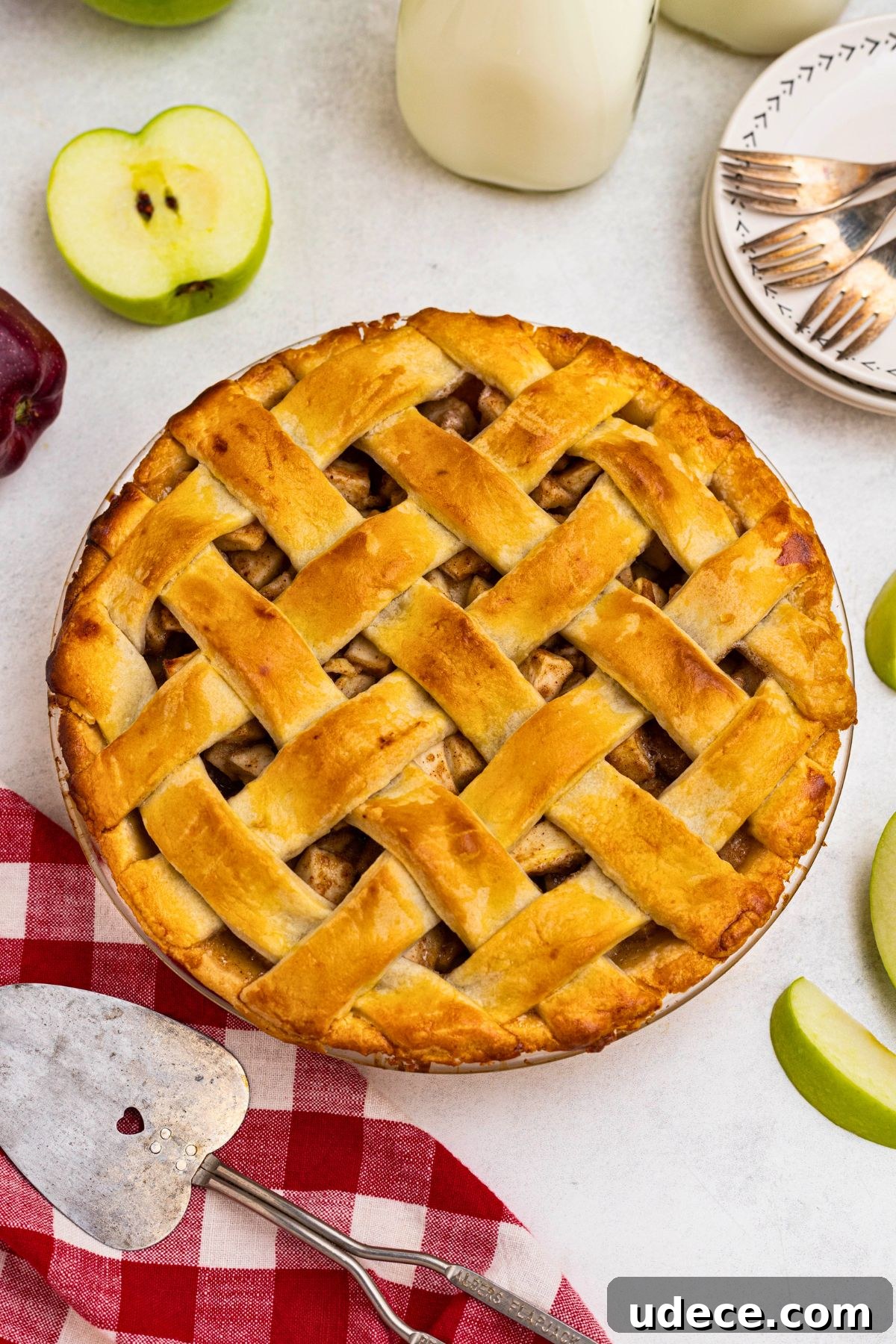 Classic Homemade Apple Pie Recipe for Perfect Crust and Filling 2 Golden crust, baked apple pie, on a white marble table, with slices of green apple, and a small plate with forks, next the whole pie.