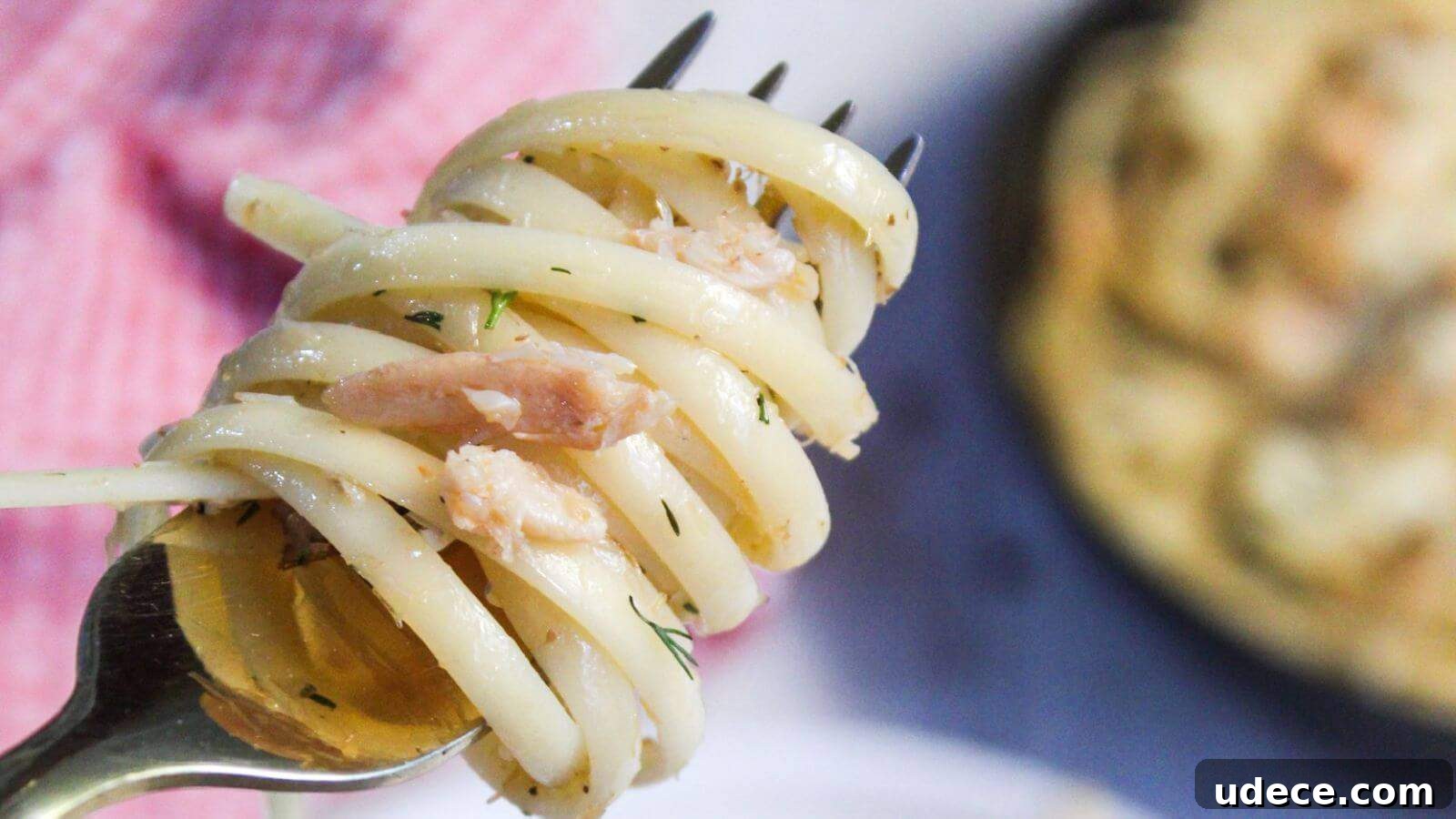 28 Seafood Dinners for Two That Deliver Restaurant-Quality Flavor 12 A fork twirling crab pasta with bits of herbs, set against a plate with more pasta and a blurred background.