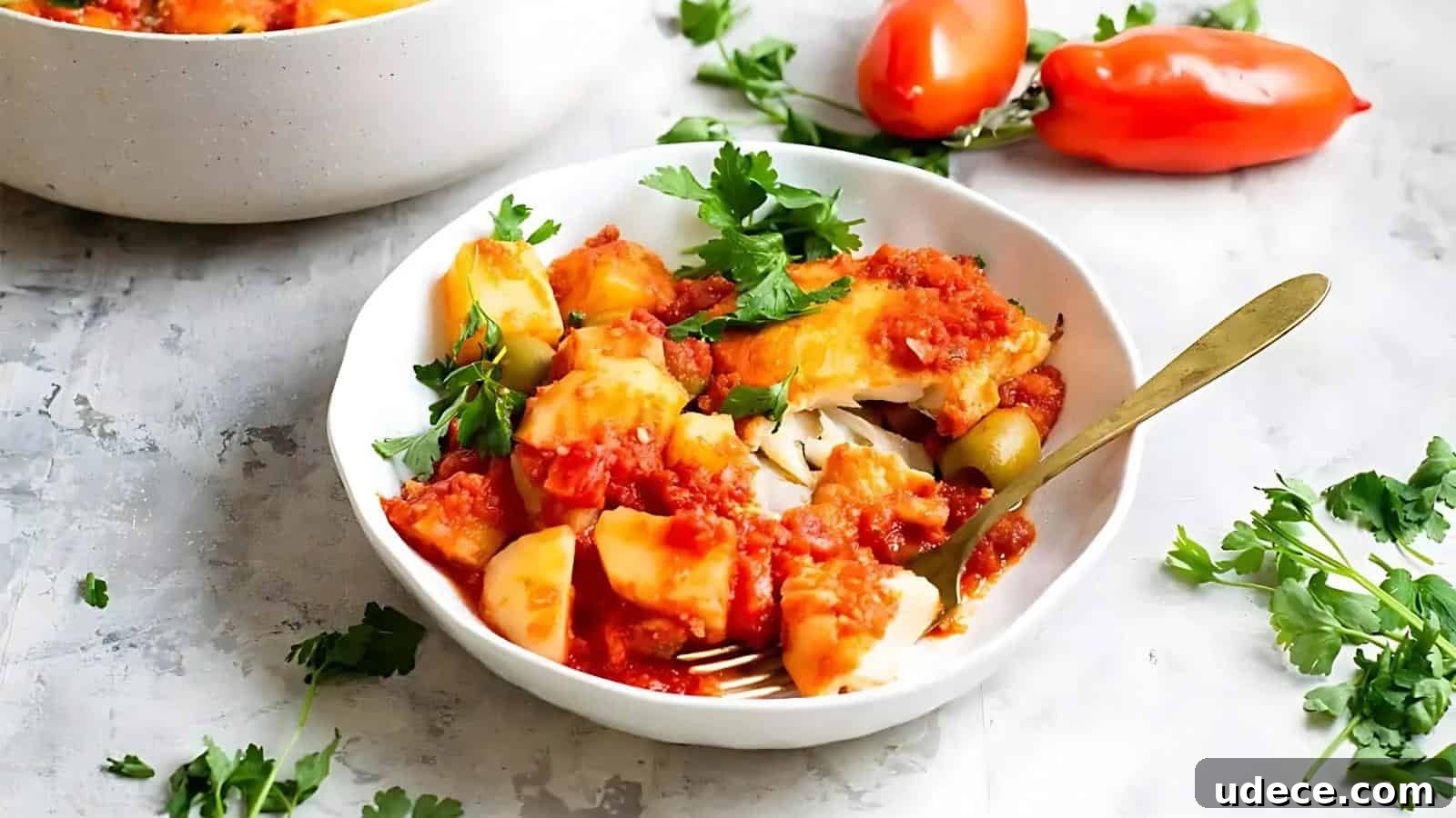 28 Seafood Dinners for Two That Deliver Restaurant-Quality Flavor 14 A white bowl filled with potatoes and fish in tomato sauce, garnished with fresh parsley, with tomatoes and parsley scattered around on a light surface. A fork is placed in the bowl.