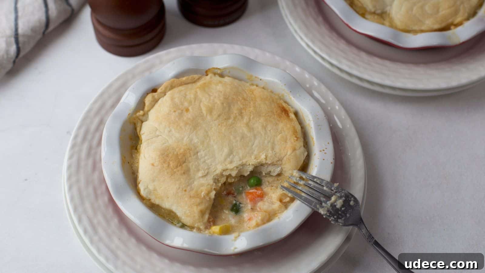 28 Seafood Dinners for Two That Deliver Restaurant-Quality Flavor 3 A seafood pot pie with a golden crust served in a white bowl, with a fork taking a bite out, revealing the creamy filling with vegetables.