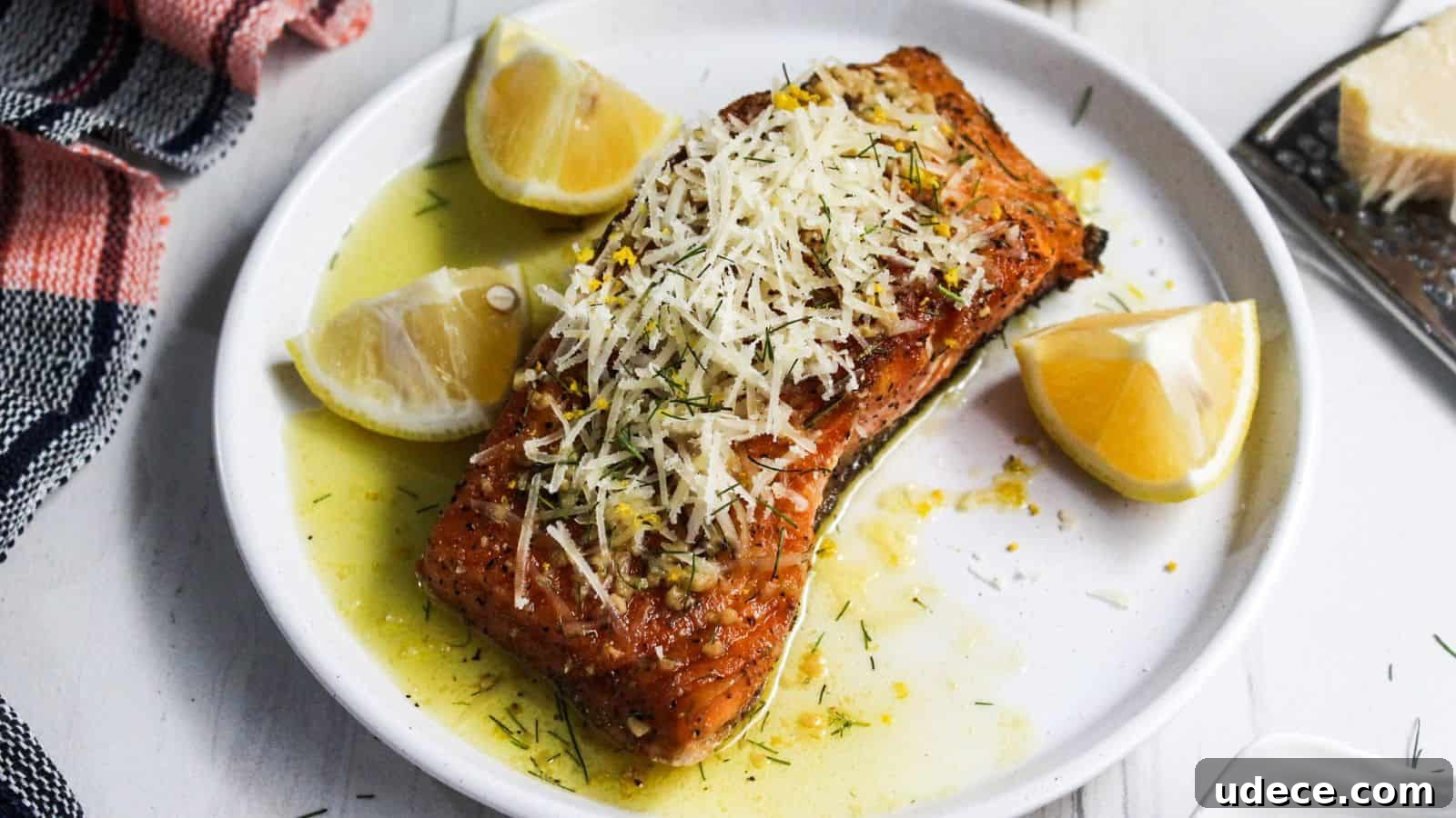 28 Seafood Dinners for Two That Deliver Restaurant-Quality Flavor 5 Grilled salmon fillet garnished with lemon slices and grated cheese on a white plate, accompanied by a red and white striped napkin.