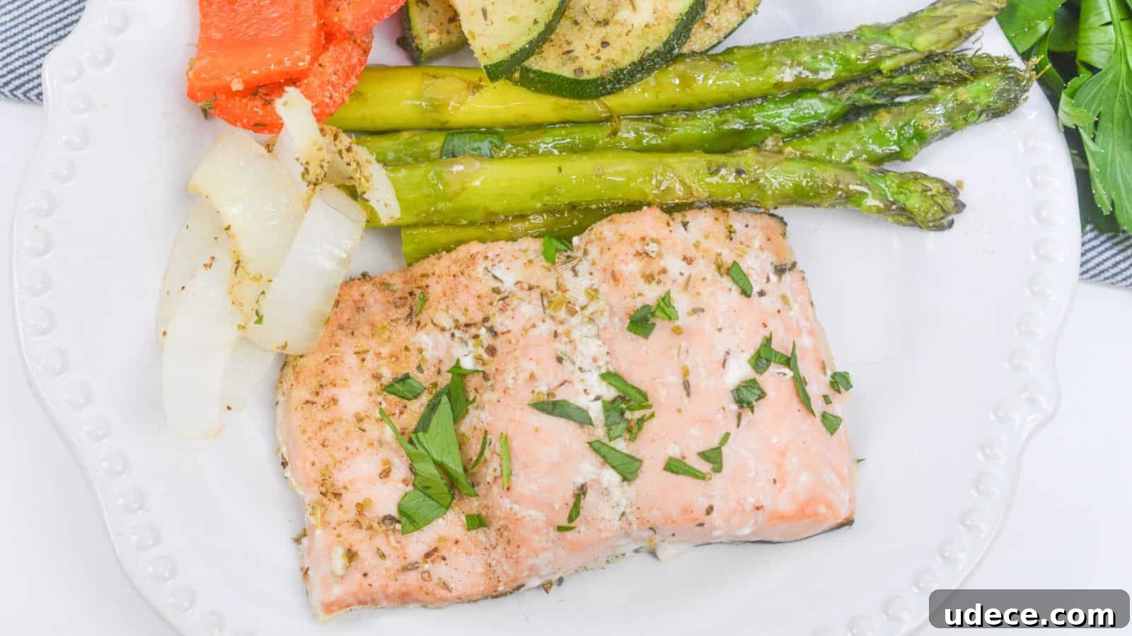 28 Seafood Dinners for Two That Deliver Restaurant-Quality Flavor 10 A plate of baked salmon garnished with herbs, served alongside asparagus, zucchini, onions, and bell peppers.