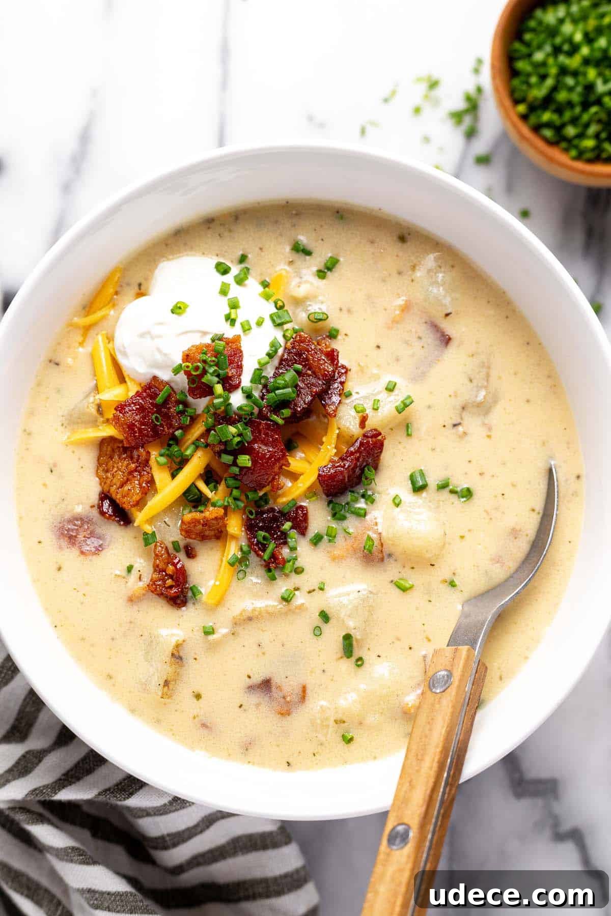 Bowl of loaded baked potato soup topped with sour cream, bacon, and shredded cheese. 