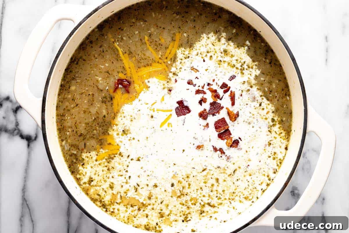 Heavy cream, bacon, and shredded cheese being added to a pot of potato soup. 