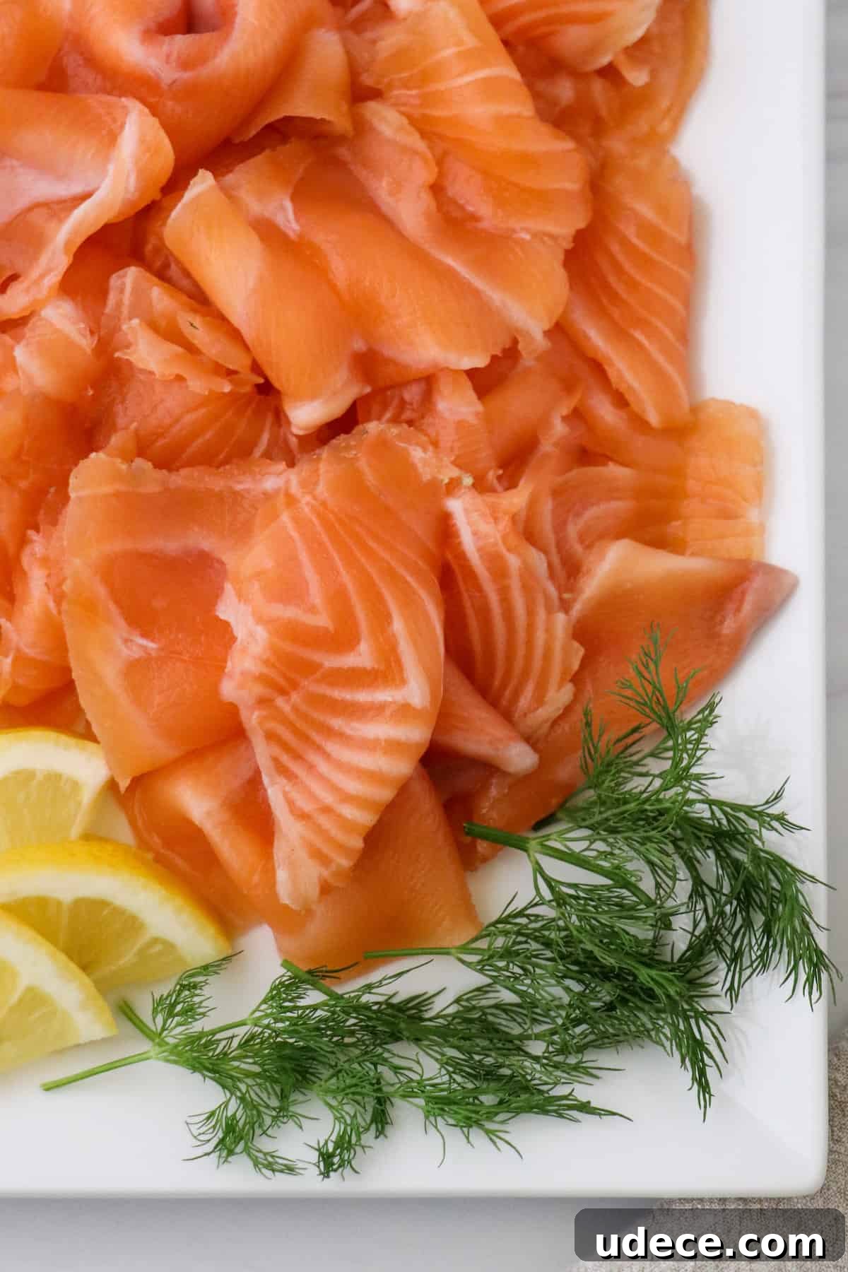 Homemade Gravlax: Simple Cured Salmon with Dill and Citrus 2 Homemade Gravlax on a square plate with dill and lemon wedges.