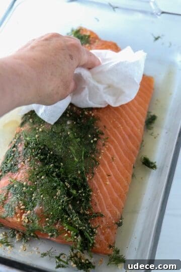 Homemade Gravlax: Simple Cured Salmon with Dill and Citrus 11 Person wiping dill off of salmon with a paper towel.