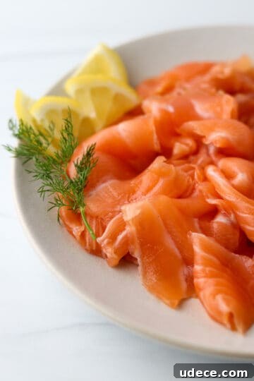 Homemade Gravlax: Simple Cured Salmon with Dill and Citrus 13 Close up of gravlax on a plate with a dill sprig and lemon wedges.