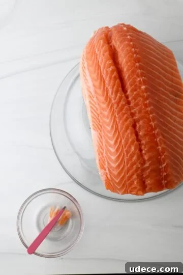Homemade Gravlax: Simple Cured Salmon with Dill and Citrus 5 Side of salmon on an overturned glass bowl next to a small bowl with tweezers.