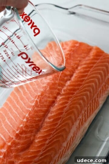 Homemade Gravlax: Simple Cured Salmon with Dill and Citrus 6 Person pouring aquavit over a salmon filet.
