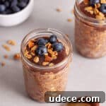 A single mason jar portion of Nutella overnight oats topped with blueberries and granola.