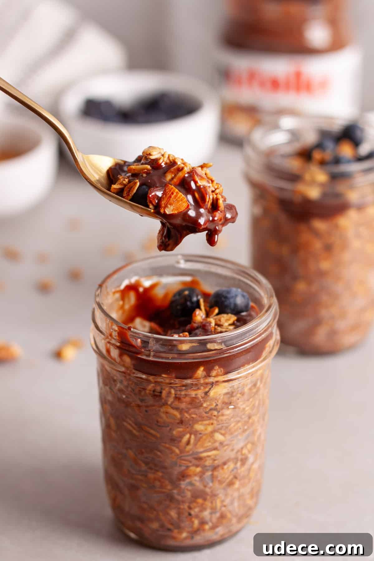 Nutella Overnight Oats Recipe for Creamy Chocolate Breakfast 9 A spoon taking a bit of chocolate overnight oats out of a small mason jar on a gray table.