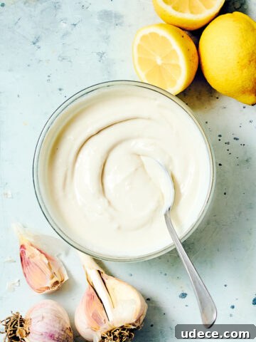 Creamy Shawarma sauce in a bowl with a spoon, with lemons and garlic.